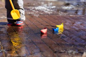 child playing with paper boats in spring water puddle