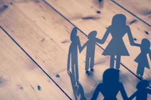 A family paper chain ring on a wooden background. The chain is made up of adult and child male and female characters.